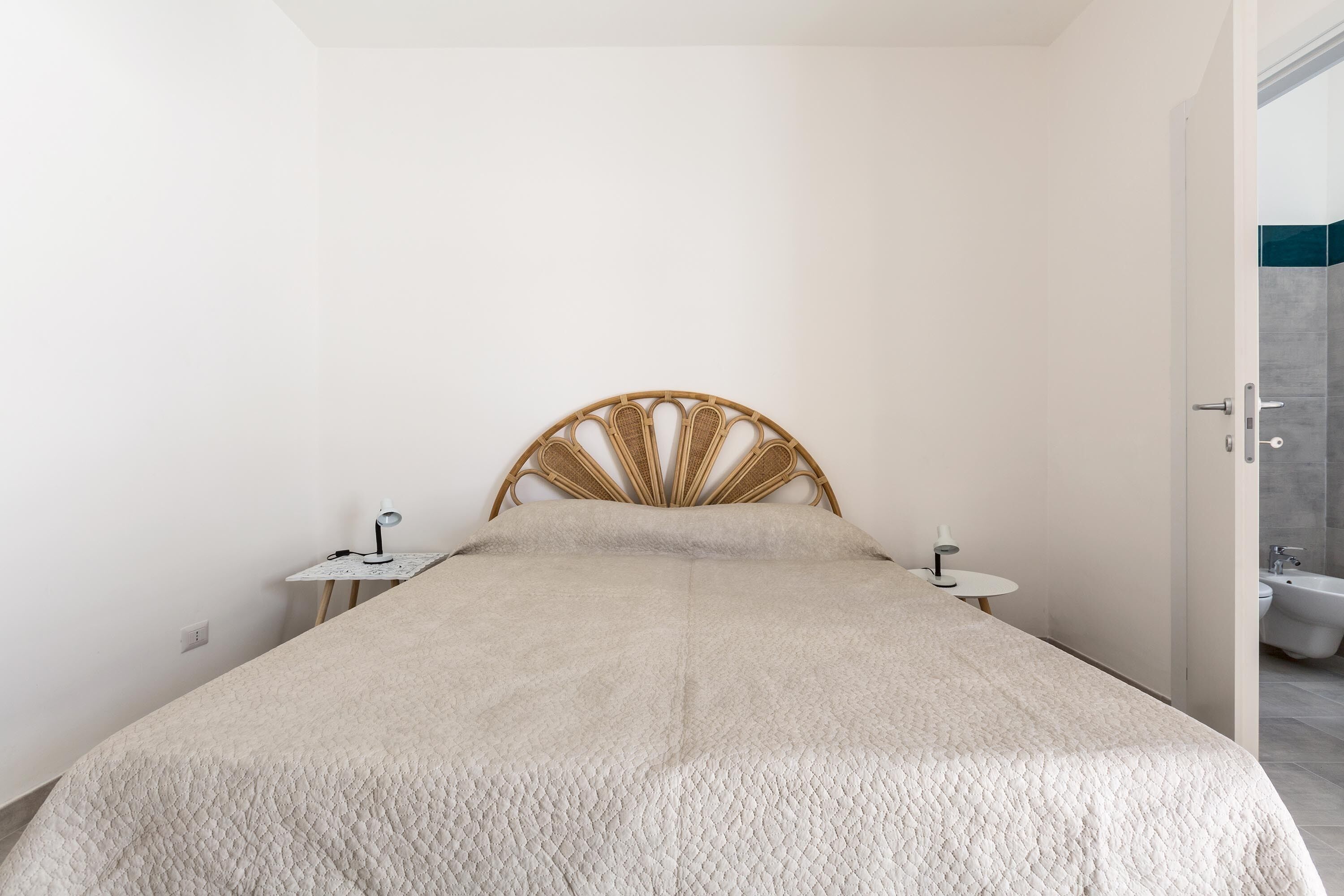 Une chambre à coucher avec un lit, une table de chevet, une commode et une salle de bain visible à travers une porte ouverte.