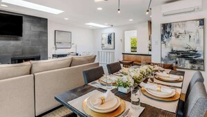 Un espace de repas moderne avec une longue table dressée pour le repas, un canapé et une cheminée.