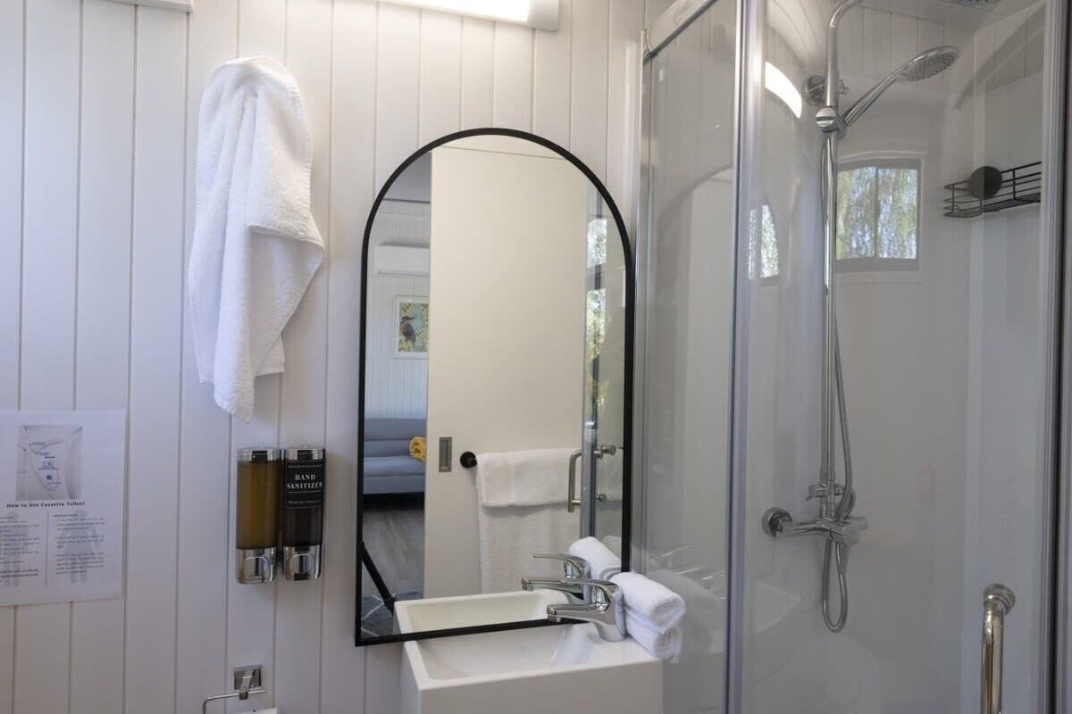 Une salle de bain avec une douche à parois de verre, un lavabo blanc, un miroir et une serviette accrochée au mur.