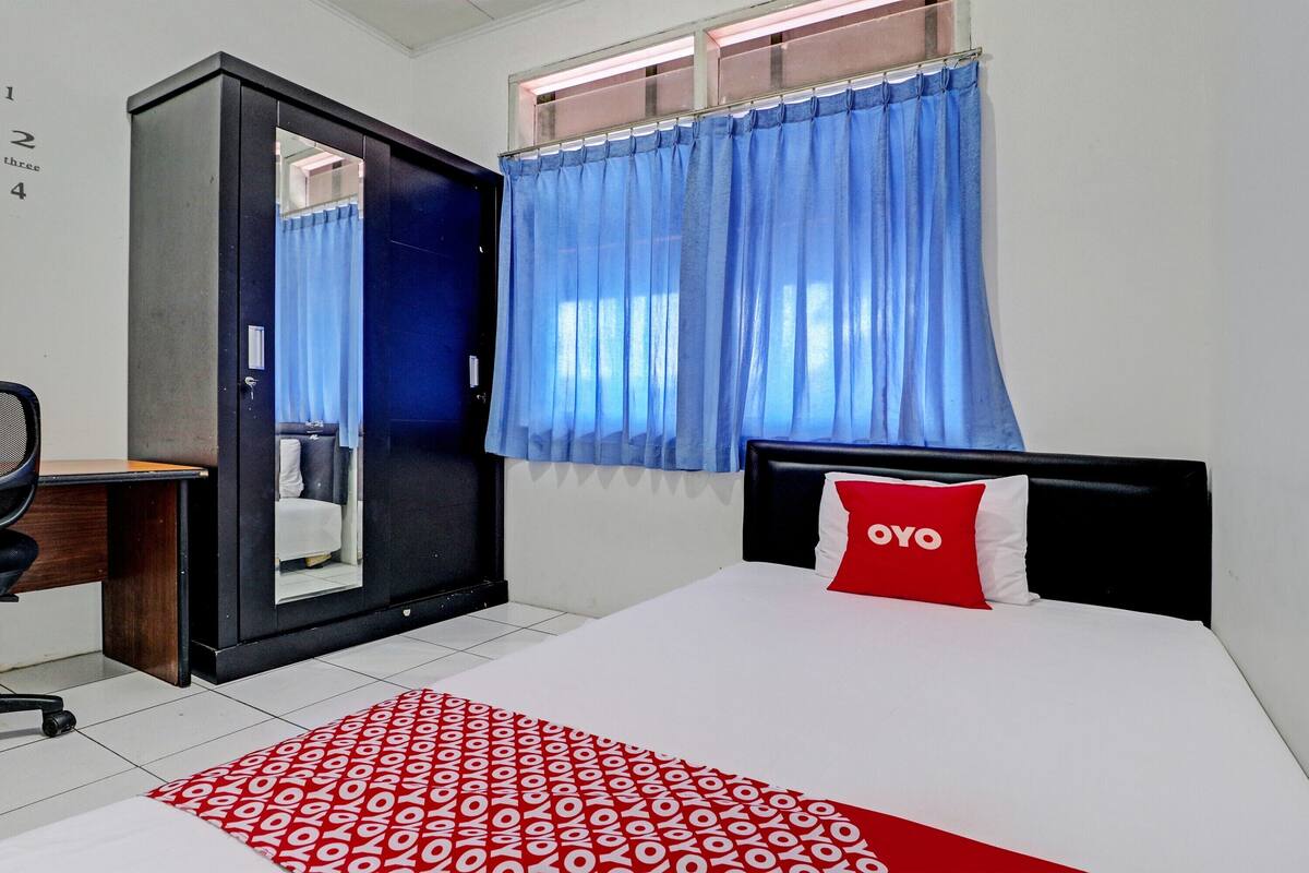 Ein Hotelzimmer mit Bett, Schreibtisch, Stuhl, Kleiderschrank und einem Fenster mit Vorhängen.