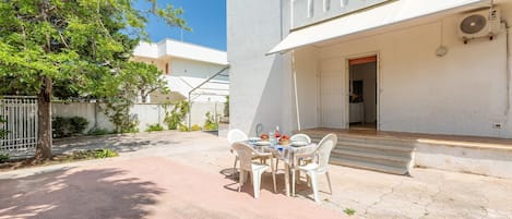 A patio with a table and chairs, a white building with a balcony, and a tree.