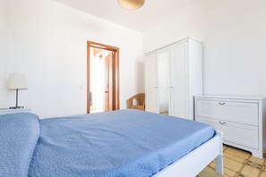 A bedroom with a bed, a nightstand, a wardrobe, and a wicker chair. - 3434 Mare Azzurro - Appartamento Ilary (Porto Cesareo)