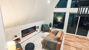 Un loft espacioso con techo alto, una zona de estar acogedora con sofá y alfombra redonda, chimenea y ventanas amplias que ofrecen vistas del interior.