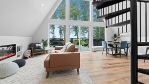 Una sala de estar moderna con chimenea, asientos y ventanas amplias que ofrecen vistas al exterior.