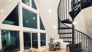 Un loft espacioso con techo alto, un ventanal grande, una escalera moderna y una zona de estar acogedora.