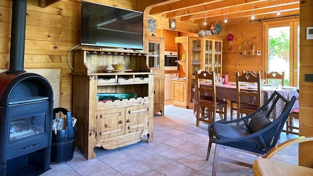 A wooden cabin interior with a TV, fireplace, wooden cabinet, dining table, chairs, and a hammock.