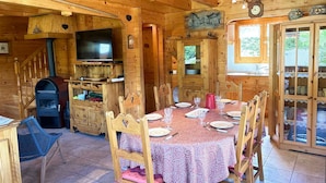 A wooden cabin with a dining area, a fireplace, a television, and a kitchen.