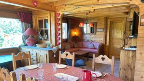 A cozy wooden cabin interior with a dining area, a sofa, and a kitchen area.