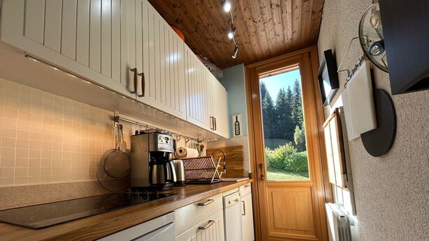 A modern kitchen with white cabinetry, a coffee machine, and a view of the outdoors through a door.
