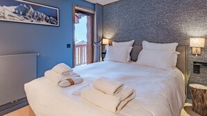Habitación de hotel moderna con una cama grande, vistas a las montañas por la ventana y un cabecero de madera.