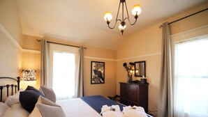 Ein Hotelzimmer mit einem großen Bett, einem Schreibtisch, einem Stuhl, einer Lampe, einem Spiegel und einem Fenster mit Vorhängen.