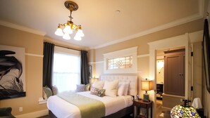 A spacious bedroom with a large bed, a nightstand, a lamp, and a painting on the wall. - Relax in the luxurious 1-bedroom Louisa Suite at RedTail Inn. Enjoy a double rain shower, plush linens, and a shared hot tub. Located near downtown Ashland, with off-street parking and high-speed WiFi. (Ashland)