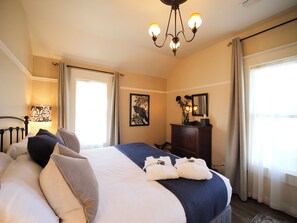 Une chambre d’hôtel avec un grand lit, un bureau, une chaise, une lampe, un miroir et une fenêtre avec des rideaux.