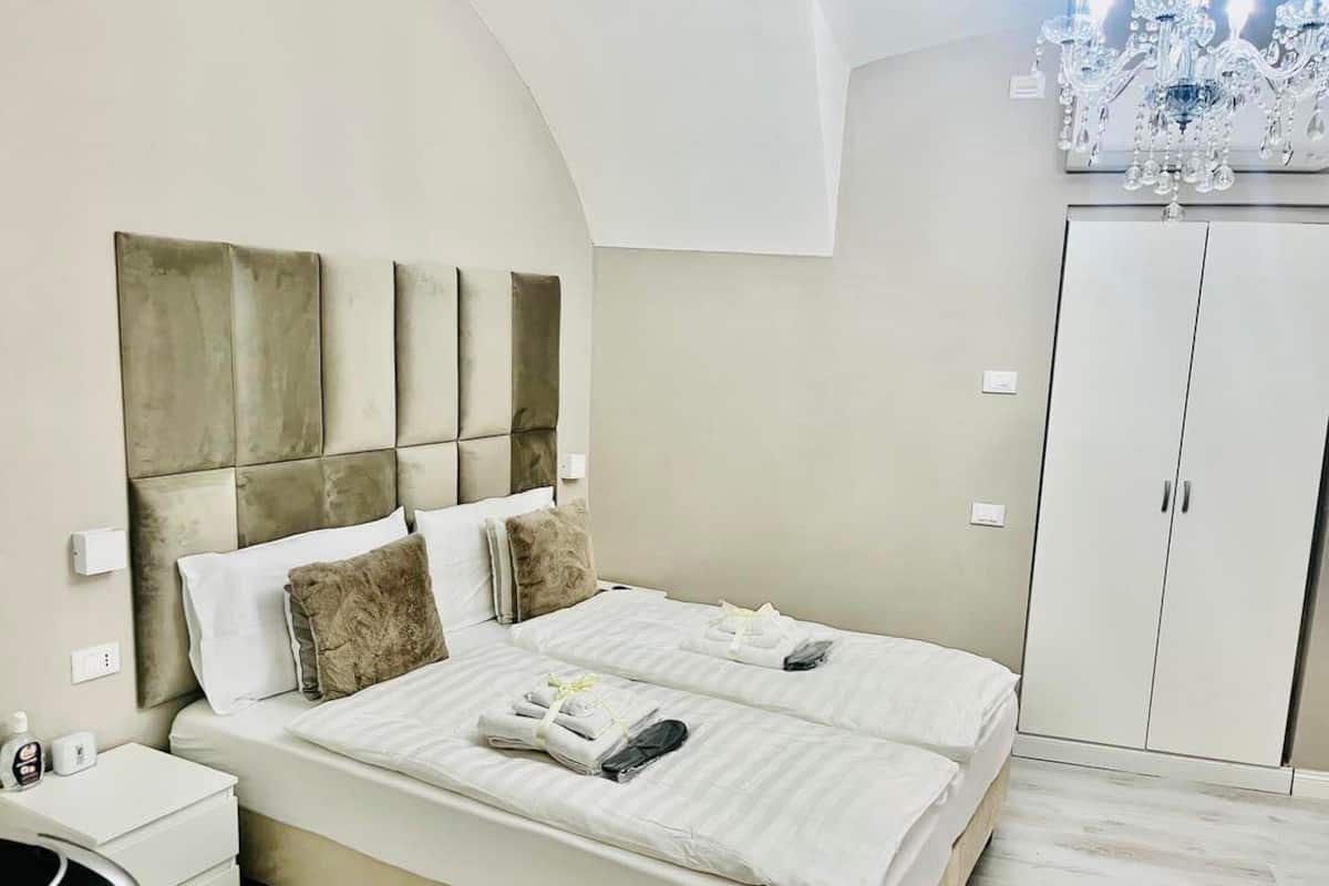 A double bed with a headboard, a bedside table, a wardrobe, and a chandelier.