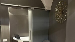 A modern room with a sliding door leading to a bathroom, a grey upholstered chair, and a decorative wall piece. - Beb C'est Lavis (Lavis)