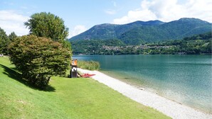 A lakeside view with a grassy area, a small dock, and a building with a red roof near the water. - Beb C'est Lavis (Lavis)
