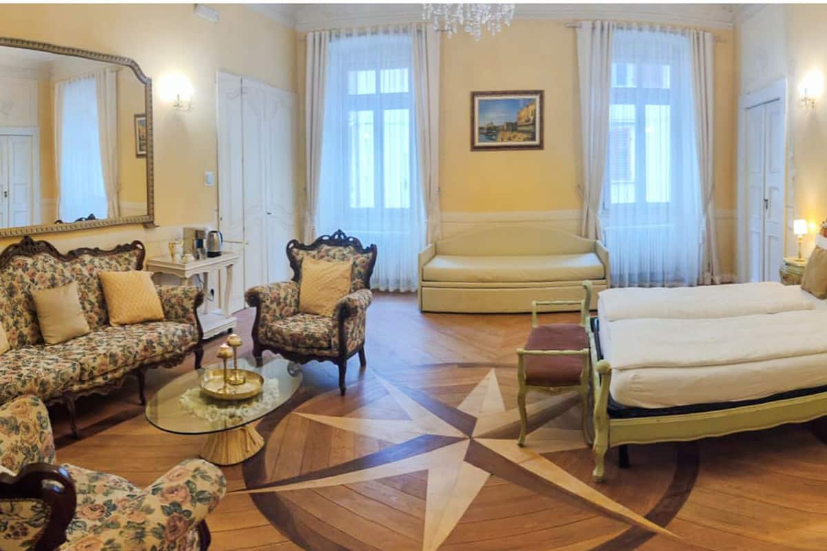 A hotel room with a large bed, two armchairs, a sofa, a small table, and a decorative mirror.