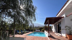 A swimming pool with a pergola and lounge chairs, surrounded by a white building and a mountain view. - Villa Ana, Chalet Independiente (AN)