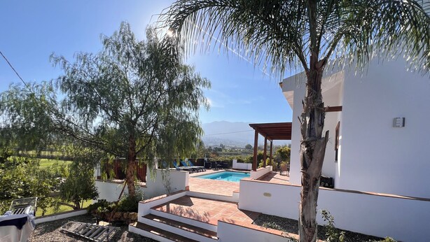 A modern outdoor pool area with a pergola, steps leading to a covered seating area, and a view of the surrounding landscape. - Villa Ana, Chalet Independiente (AN)