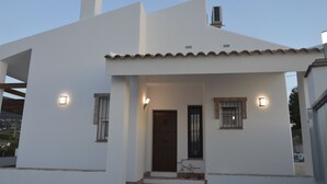 A white building with a tiled roof, a wooden door, and two windows with metal bars. - Villa Ana, Chalet Independiente (AN)