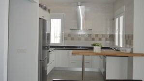 A modern kitchen with white cabinets, a stainless steel refrigerator, a wooden countertop, and a window with blinds. - Villa Ana, Chalet Independiente (AN)