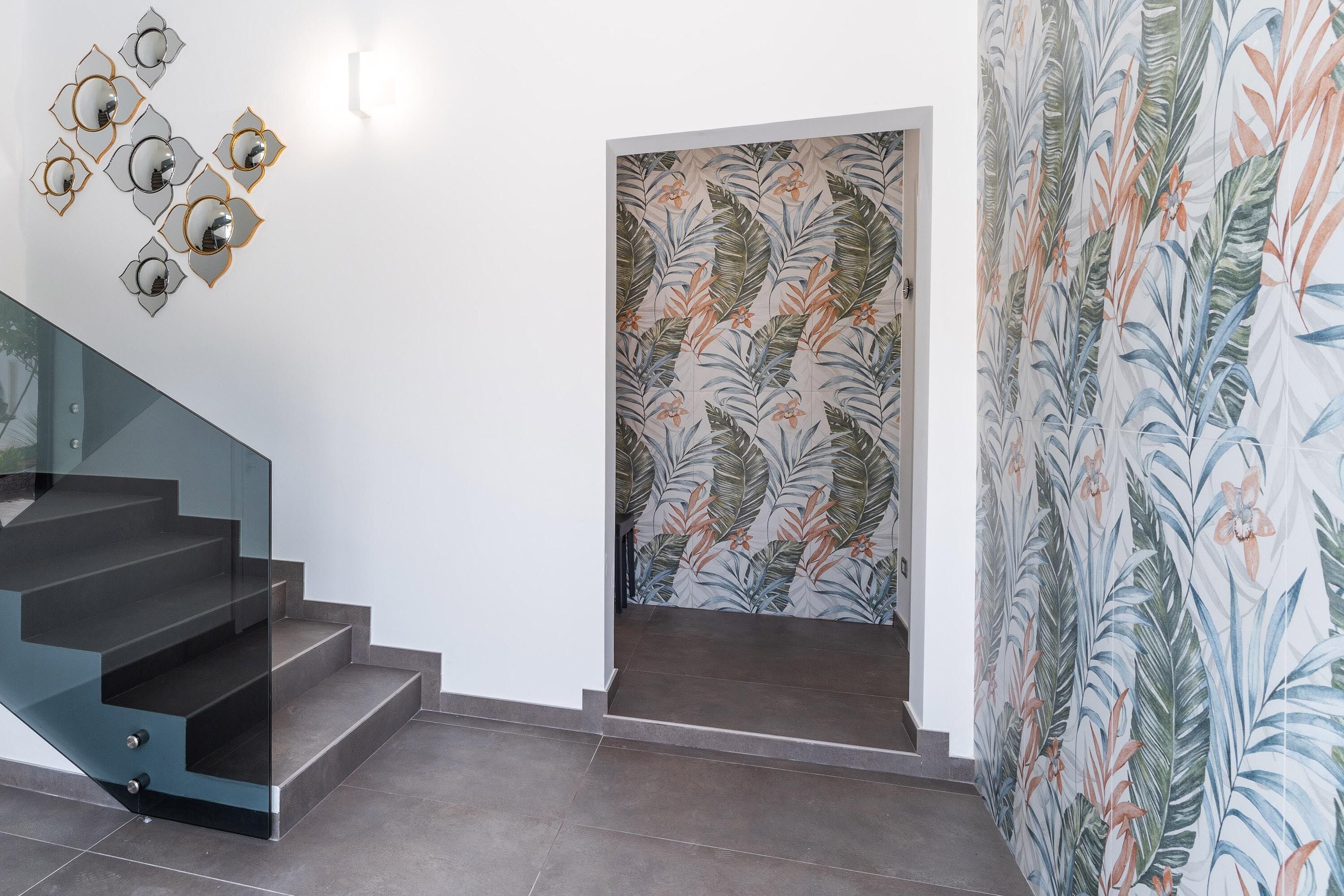 A modern staircase with glass railings and a wall with a tropical leaf pattern.