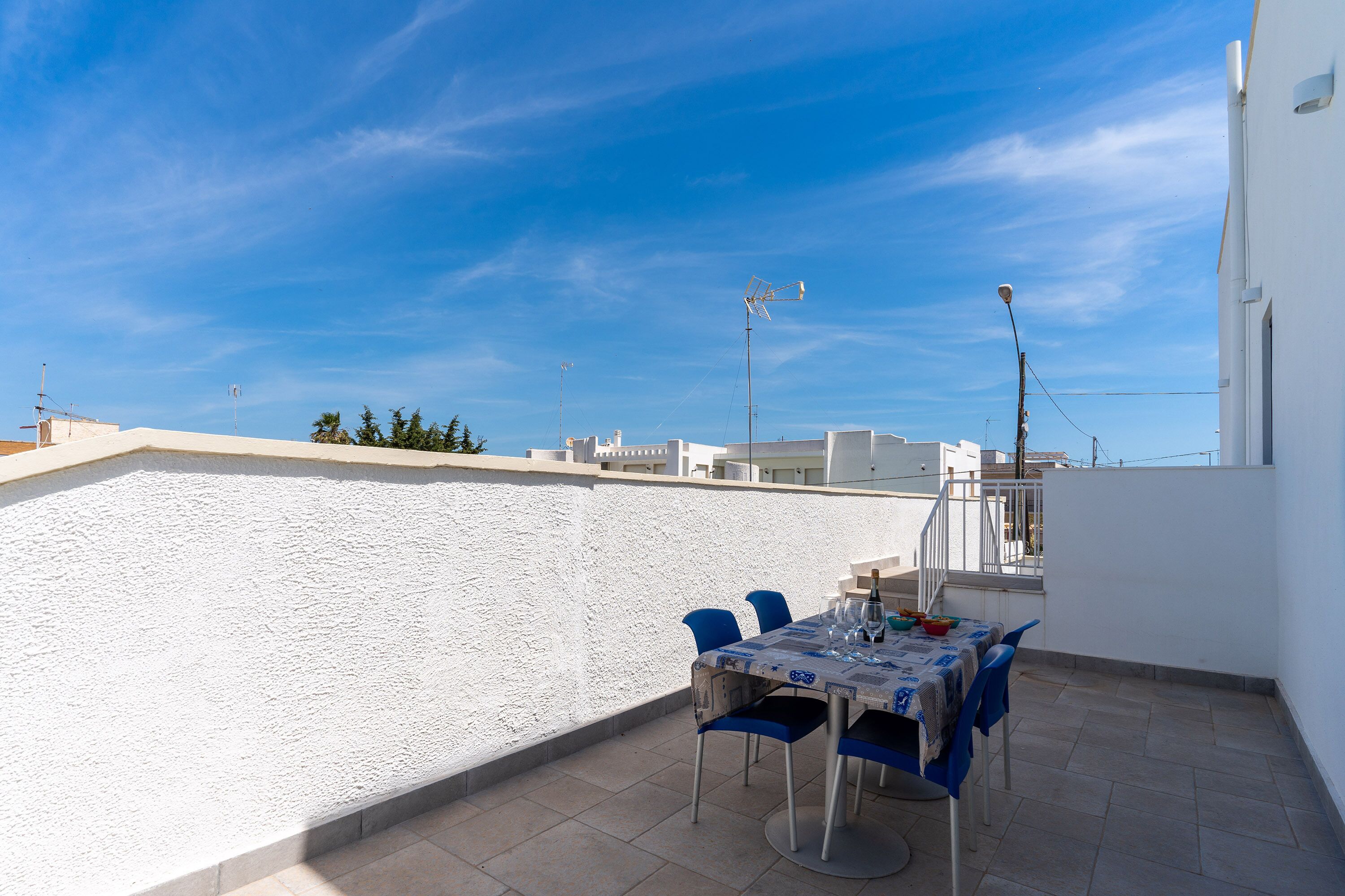 A rooftop terrace with a table set for dining, chairs, and a clear view of the sky.