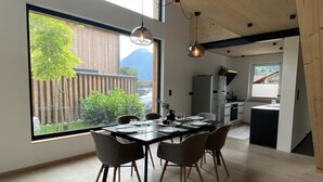 Ein moderner Essbereich mit großem Fenster, einer Küche im Hintergrund und einem Esstisch, gedeckt für vier Personen.