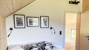 Ein Schlafzimmer mit Holzbalkendecke, einem Bett mit weißer Bettwäsche, drei gerahmten Bildern an der Wand und einer Tür zu einem anderen Raum.