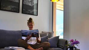 A person sitting on a grey sofa with a book, a small table with books and a vase of flowers, and two black pendant lights above.
