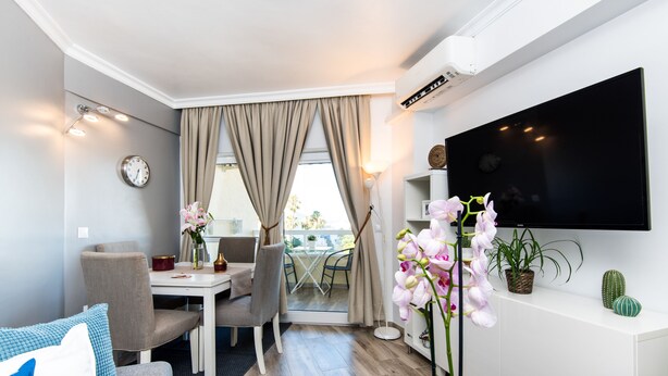 A modern hotel room with a dining area, a flat-screen TV, and a balcony with a view. - Beautiful Beachfront Apartment In Puerto Marina (Benalmádena)
