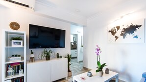 A modern living room with a flat-screen TV, white cabinetry, a bookshelf, a coffee table, and a world map on the wall. - Beautiful Beachfront Apartment In Puerto Marina (Benalmádena)