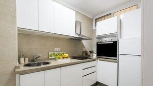 A modern kitchen with white cabinets, a stainless steel sink, a built-in oven, and a black refrigerator. - Beautiful Beachfront Apartment In Puerto Marina (Benalmádena)