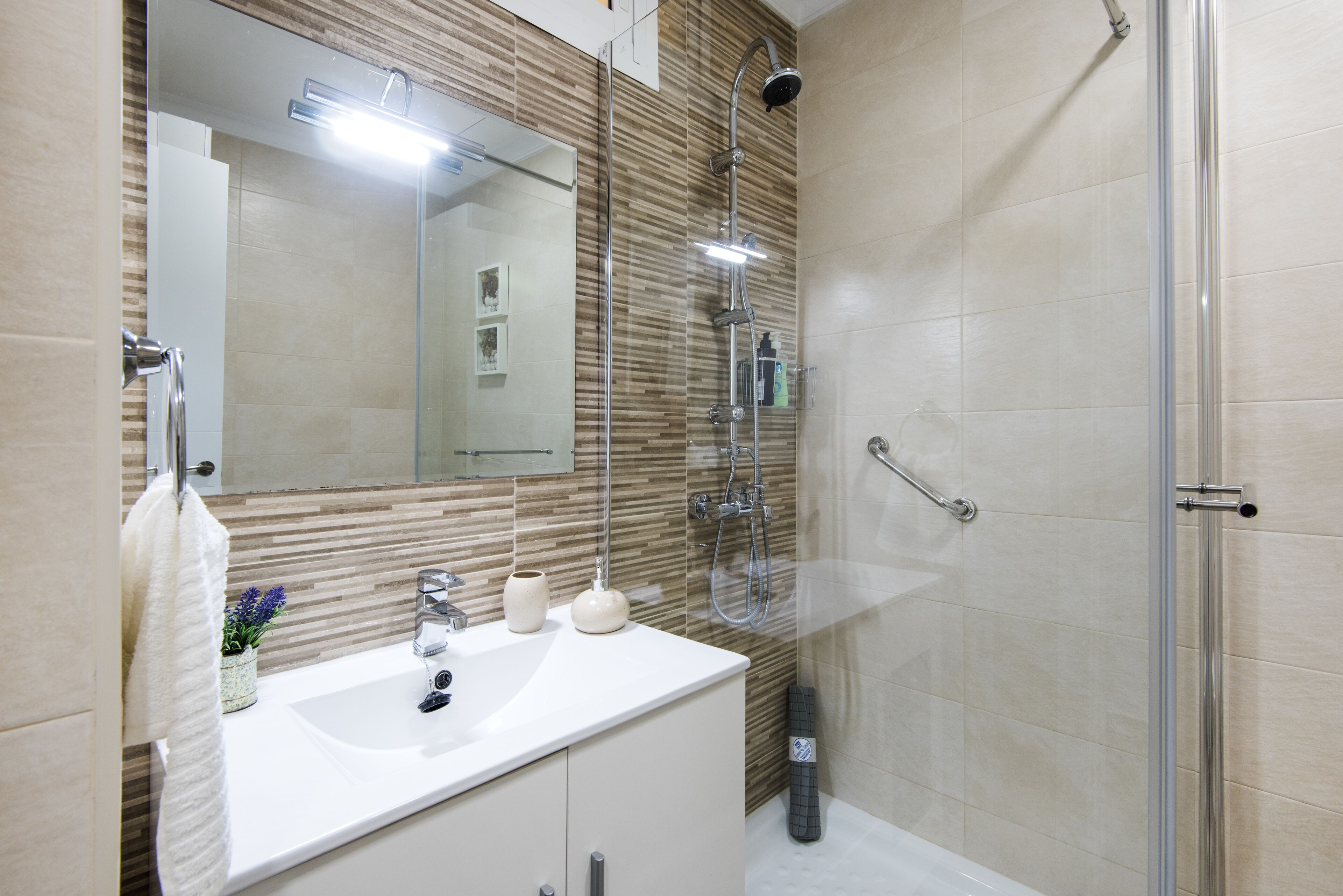 A modern bathroom with a glass shower enclosure, a white sink, and a mirror above it.