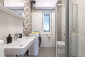 Enjoy a refreshing shower in the bathroom with a glass-enclosed shower, dual sink, and washing machine.