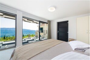 Relax in a spacious room with a large bed and sliding glass door leading to an outdoor terrace with a panoramic mountain view.