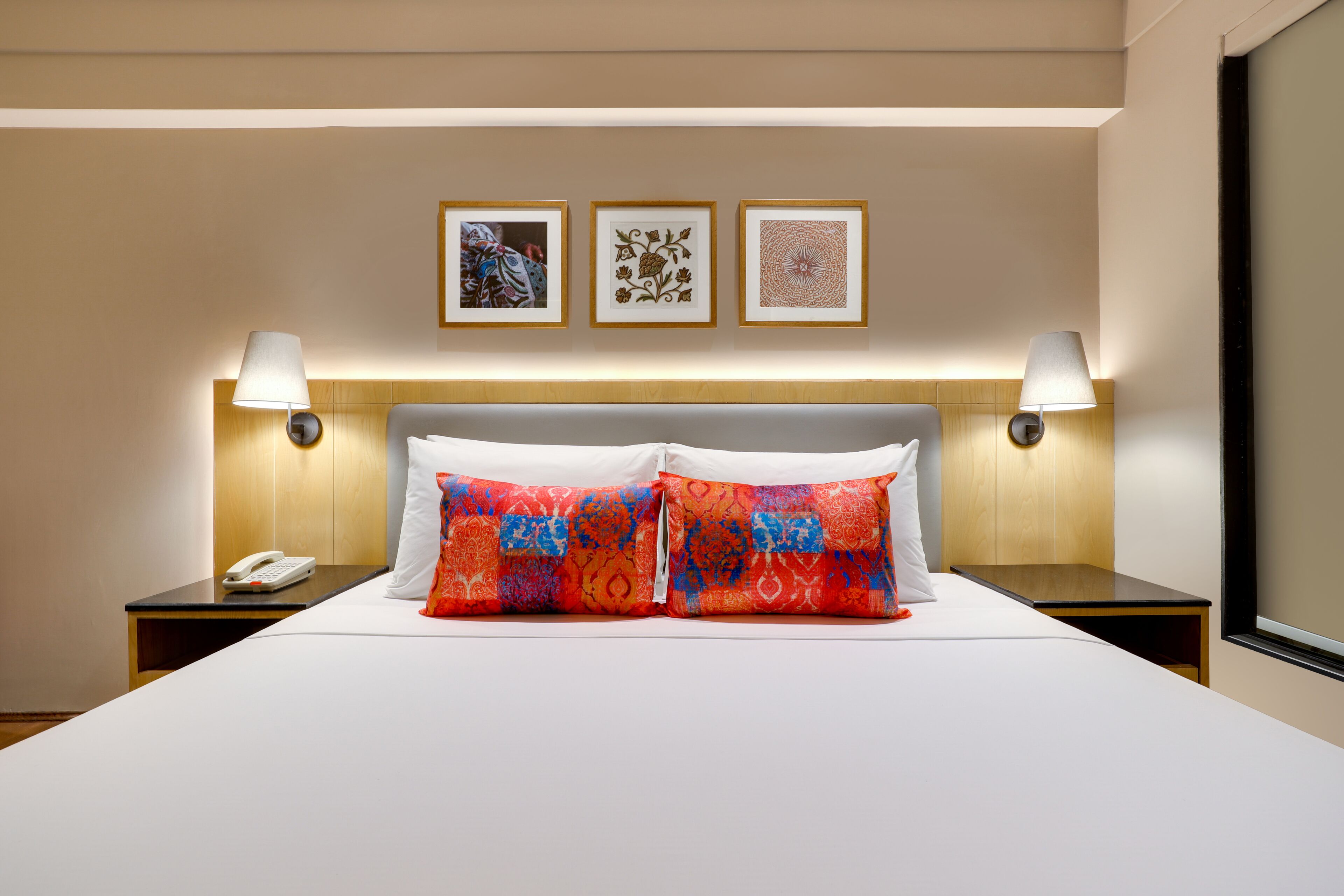 A hotel room with a large bed, two bedside lamps, a phone on the nightstand, and three framed pictures on the wall.