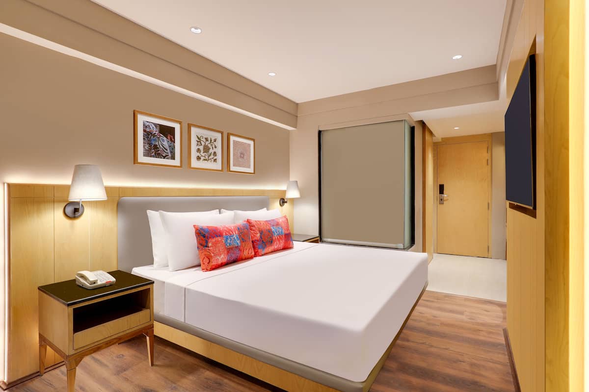 Habitación de hotel con una cama grande, lámparas de noche, mesita de noche y cuadros en la pared.