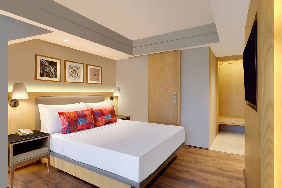 Una habitación de hotel moderna con una cama grande, lámparas de noche, un armario de madera y obras de arte enmarcadas en la pared.