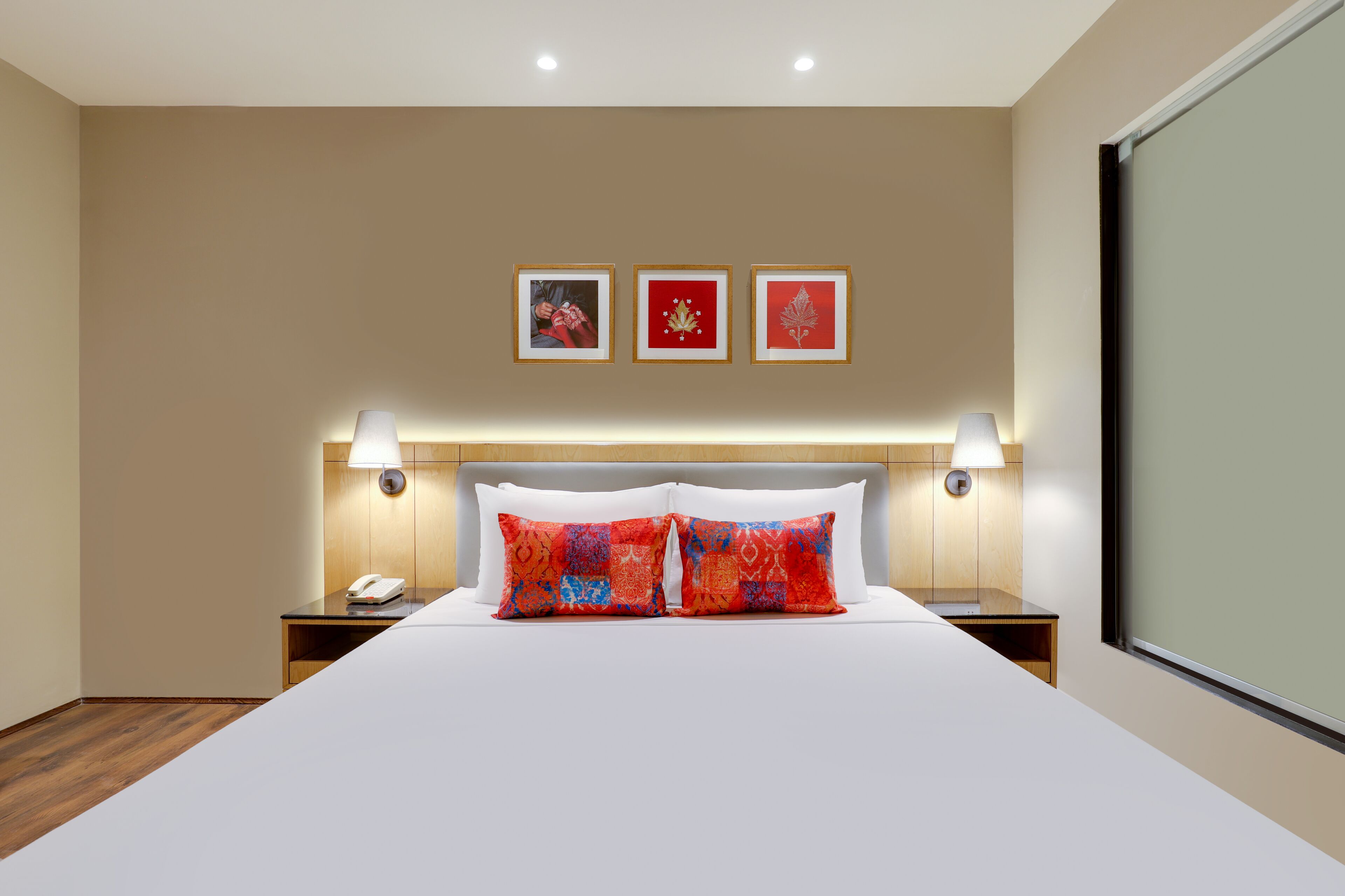 A hotel room with a large bed, two bedside tables, a telephone, and three framed pictures on the wall.