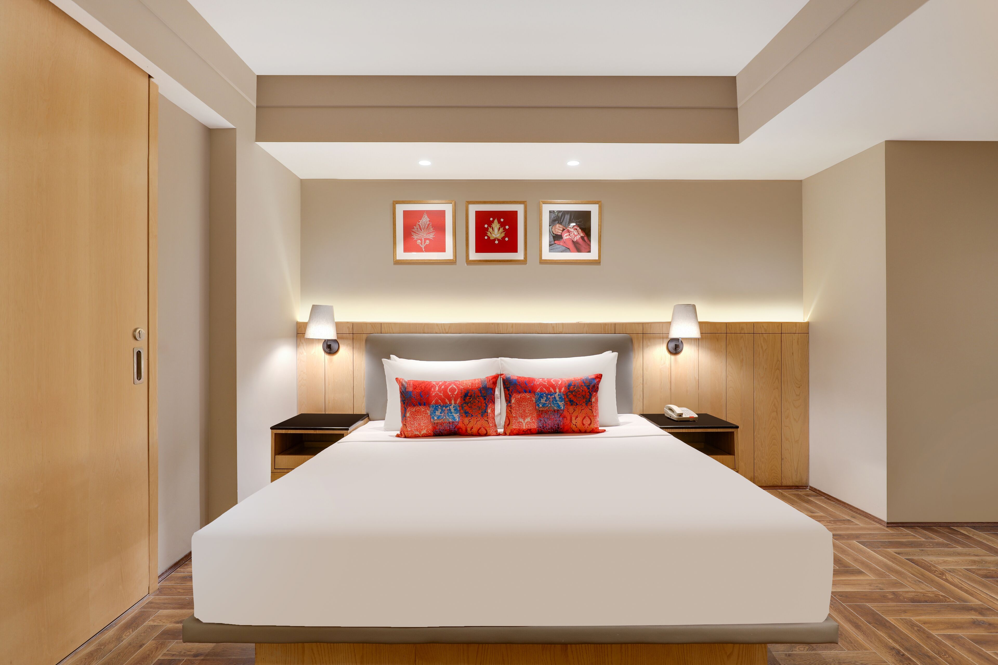 A hotel room with a large bed, two bedside tables, a wooden wardrobe, and three framed pictures on the wall.
