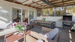 Eine Terrasse im Freien mit einem Holztisch, einem Grill und einer Sitzecke mit einer Couch und Stühlen.