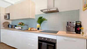 Eine moderne Küche mit weißen Schränken, einer Fischgräten-Fliesenrückwand, einer Edelstahl-Dunstabzugshaube, einer Kaffeemaschine und einem Geschirrspüler.