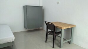 Een kleine kamer met een enkel bed, een houten tafel, een stoel en een grijze kast.