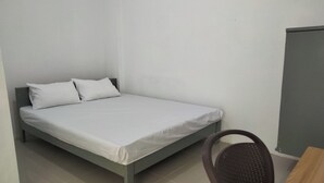 Een enkel bed met wit beddengoed in een kamer met effen witte muren en een donkerbruine stoel.
