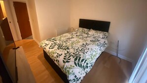 A small, clean room with a bed, a wooden floor, and a white door. - Immaculate 1-bed Apartment in Birmingham (Birmingham)