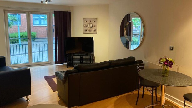 A modern living room with a sofa, a TV, and a dining table with chairs. - Immaculate 1-bed Apartment in Birmingham (Birmingham)