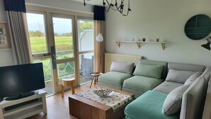 Ein Wohnzimmer mit einer Couch, einem Couchtisch, einem Fernseher und Blick ins Freie.