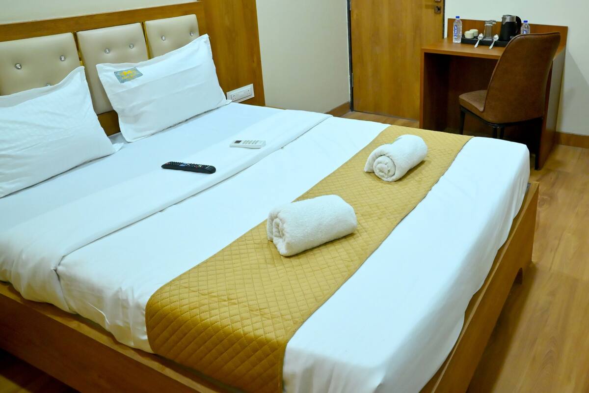 A neatly made bed with white linens and a yellow quilted bedspread, a remote control, and a rolled towel on the bed.