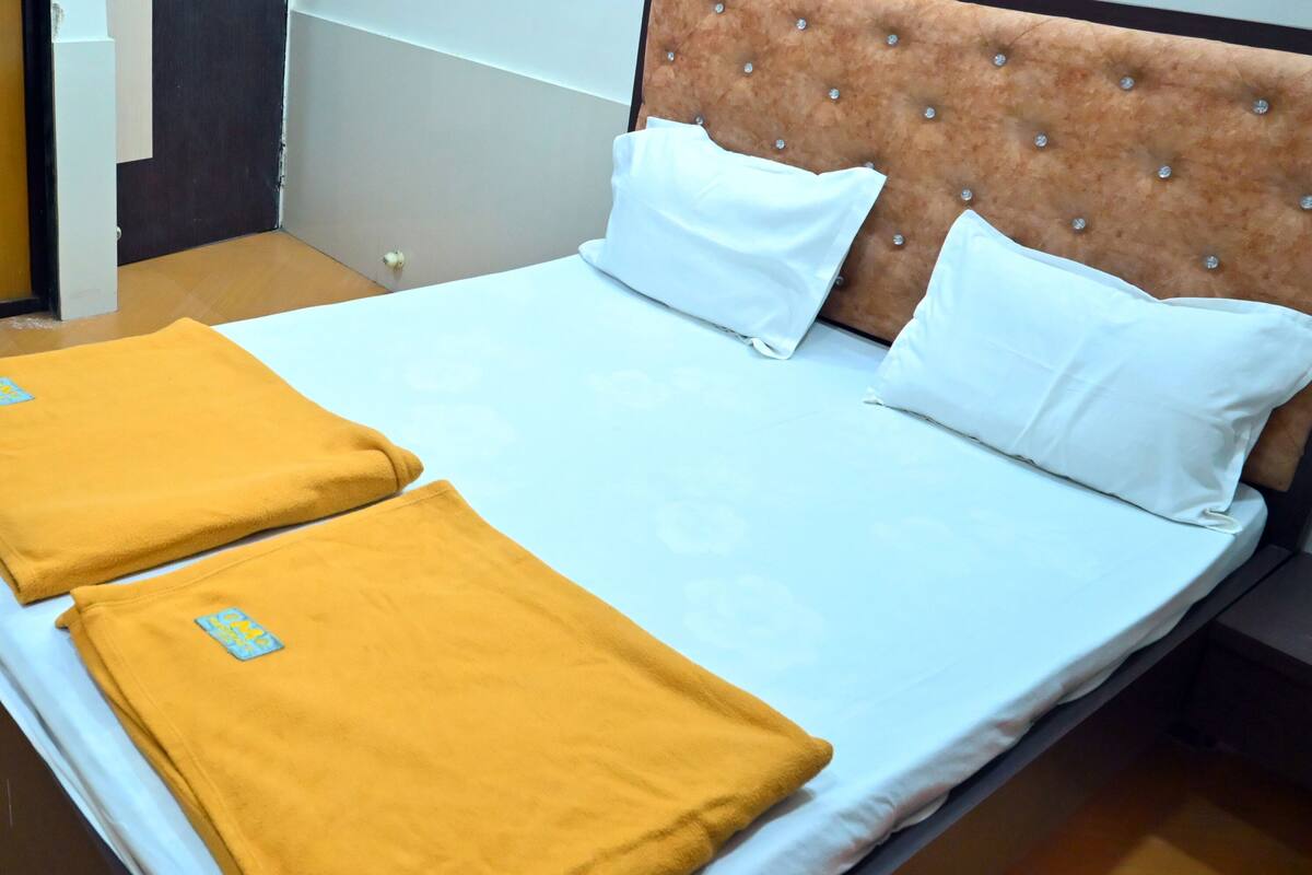 A neatly made bed with white and yellow linens, a tufted headboard, and a small logo on the pillows.